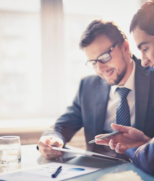 Image of two young businessmen using touchpad at meeting